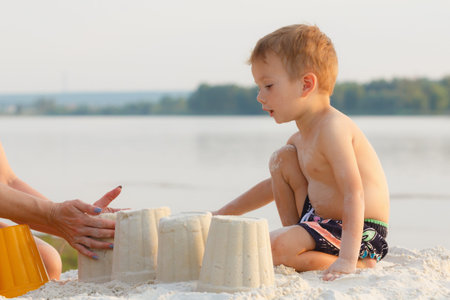 Little baby boy is resting on the sandy shore and build a castleの写真素材