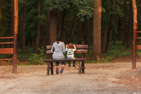 Cute little boy with his mother sitting on a park benchの写真素材