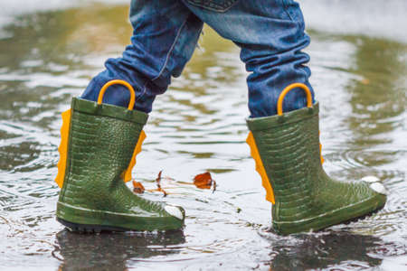 child with rain boots jumps into a puddle with leaf, autumn conceptの写真素材
