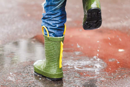 child with rain boots jumps into a puddle with leaf, autumn conceptの写真素材