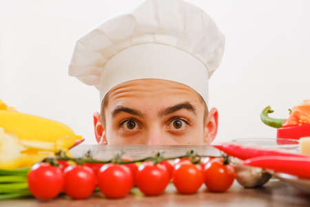 Man with cook cap on white background. Homemade food concept. Chef with vegetables on table. Cook with cheerful face in face close up.の写真素材
