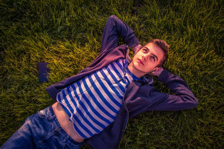 Teenage boy lying on grass with phone and listens to musicの写真素材
