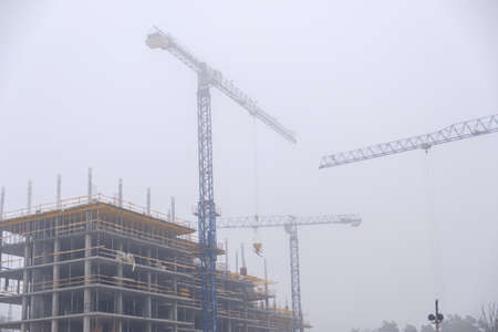 Crane on the background of under construction skyscrapers in a fog on an abandoned construction siteの写真素材
