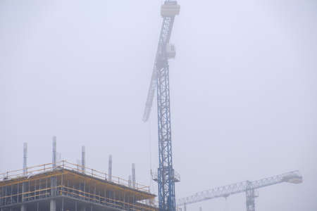 Crane on the background of under construction skyscrapers in a fog on an abandoned construction siteの写真素材