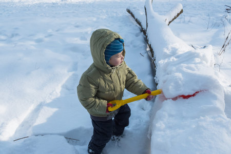 Happy child in winterwear laughing while playing in snowdrift outside