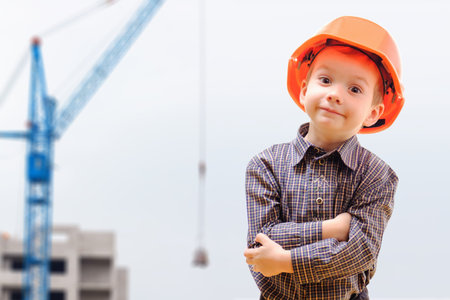 Concept, small boy in a helmet, looking at construction site with cranesの写真素材