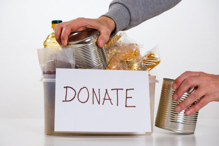 Food in a donation cardboard box, isolated on white background, volunteer fills the box.