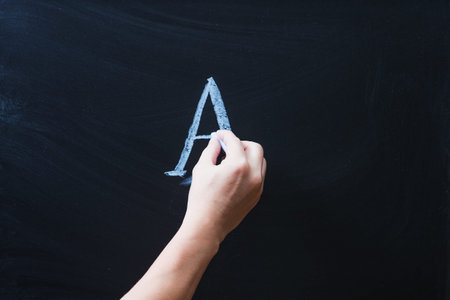 Female hand writing alphabet on black chalkboard. Educational background with ABC letters and copy...