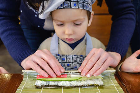 Cooking, Preparation of traditional sushi rolls. The boy is dressed as a cook.の写真素材