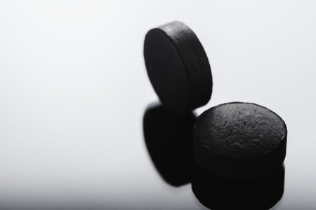Black Pill tablet medicine lying isolated on white background extreme close-up macro.