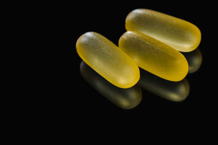 Heap of yellow capsule pills tablets medicine lying isolated on black background extreme close-up macro.の写真素材