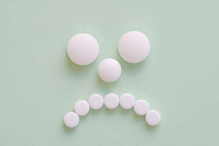Sad patient face made from white round pills on green backgroundの写真素材