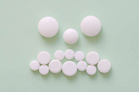 Sad patient face made from white round pills on green backgroundの写真素材