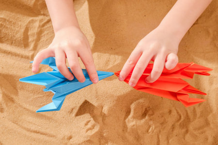 Happy child boy playing with handmade origami paper rocket on beach sand