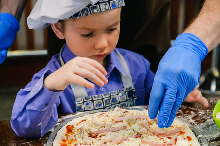 Children make pizza. Master class for children on cooking Italian food. Learn to cook a pizza kid preparing, little cook. Hands of people making pizzas togetherの写真素材