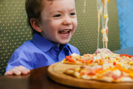 Laughing smiling cheerful child, boy, eating pizza at a restaurant, summertimeの写真素材