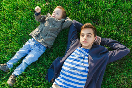 Two boys lying on the grass listing music in the parkの写真素材
