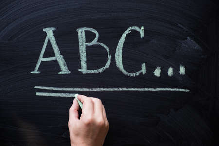 Female hand writing alphabet on black chalkboard. Educational background with ABC letters and copy spaceの写真素材