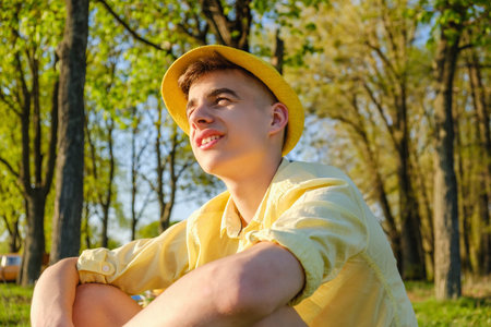 A portrait of a happy teenage boy outside, wearing a yellow shirt and hat against a blue sky and...