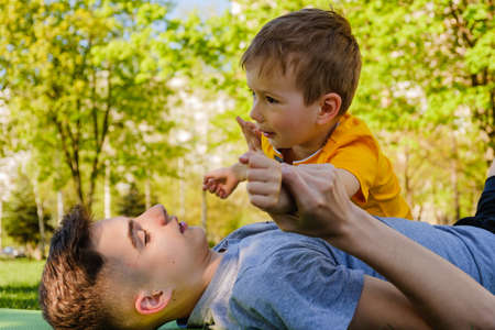 Cheerful two brothers lie on the grass in the park and play in funny games smilingの写真素材