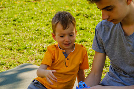 Cheerful two brothers lie on the grass in the park and play in funny games smilingの写真素材