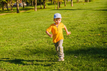 Cute boy runs along the green grass in spring or summer in a park in nature. Active rest of children.の写真素材