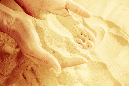 Close-up of female hand releasing dropping sand. Sand flowing through the hands. Summer beach holiday vacation conceptの写真素材