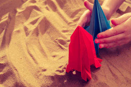 Happy child boy playing with handmade origami paper rocket on beach sand, start up conceptの写真素材