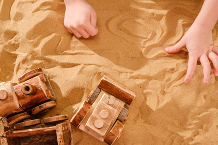 Toddler child hands playing with wooden toy tractor bulldozer model on sand of sea beach