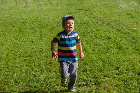 Young boy runs in a green field. Cute child running across park outdoors grass, smiling.の写真素材