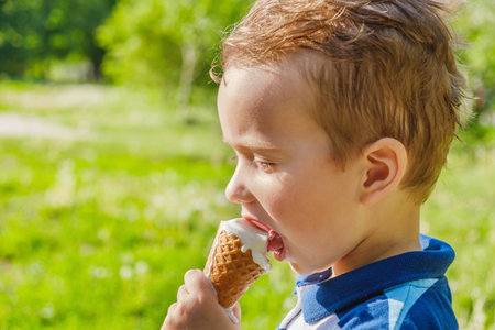3 year old caucasian boy enjoying a melting ice cream on a sweltering hot summer day. Green summer...