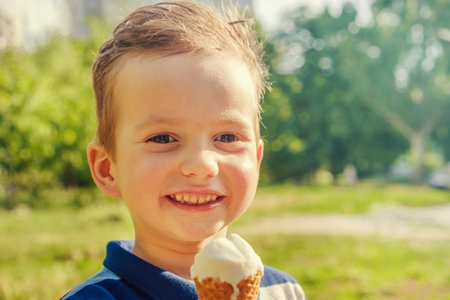 3 year old caucasian boy enjoying a melting ice cream on a sweltering hot summer day. Green summer...