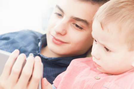 The children are smiling, looking at the display of the mobile phone. Two brothers lying playing a game or watch tv movieの写真素材