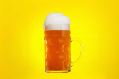 Mug of beer close-up with froth over yellow, backgroundの写真素材