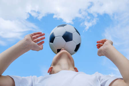Teenage boy with a soccer ball on a background of blue skyの写真素材