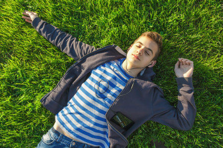 young boy lying on the green meadow with smartphone and listens to music
