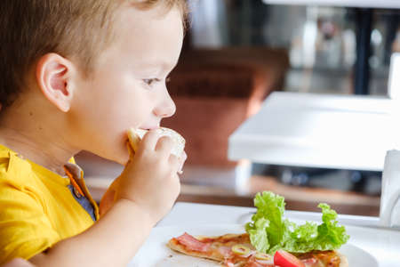 Little cute boy eating a small pizza, very eagerlyの写真素材