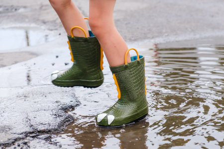 Child in a green boots jumping in puddles. A boy stands in rain, a bright raincoat. Kid playing...