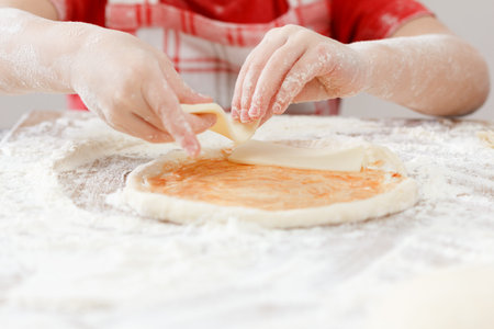 Cook putting salami over mozzarella and tomato on a raw pizza close-upの写真素材