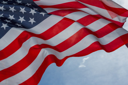 Waving in the wind star-stripped American flag against the blue sky.