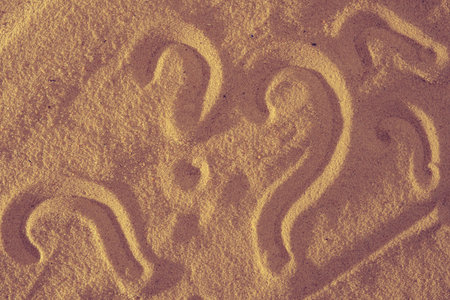 Question What and question mark symbols handwritten in white sand beach