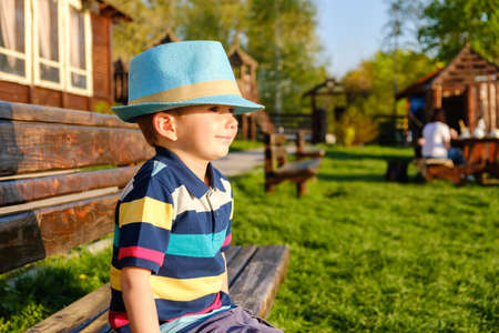Smiling child sitting on a park bench with green meadow on the backgroundの写真素材