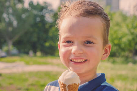 3 year old caucasian boy enjoying a melting ice cream on a sweltering hot summer day. Green summer trees in backgroundの写真素材