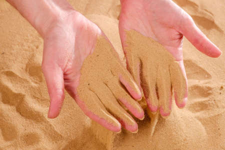 Close-up of female hand releasing dropping sand. Sand flowing through the hands. Summer beach holiday vacation conceptの写真素材