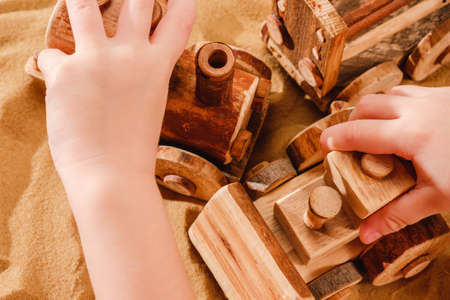 Toddler child hands playing with wooden toy tractor bulldozer model on sand of sea beachの写真素材
