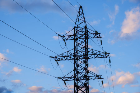 High voltage power pylons against blue sky and sun rays