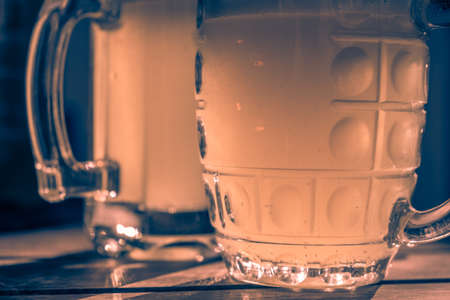 Close-up two cold beers with foam and water drops on old wooden table outdoor with sun beam, vintage colors.の写真素材