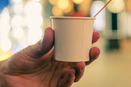 Barista is holding in hands hot cappuccino in white takeaway paper cup. Coffee take away at cafe shopの写真素材
