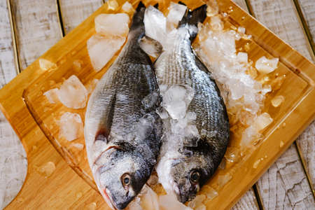 Fish seafood dorado, raw food on cutting board, wooden.Fish seafood dorado raw with ice, cold frosen food on cutting board, diet.の写真素材