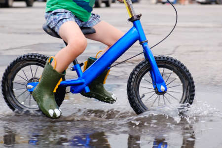 child on a balance bicycle at asphalt road in summer. Bike in the park moving through puddle on rainy dayの写真素材